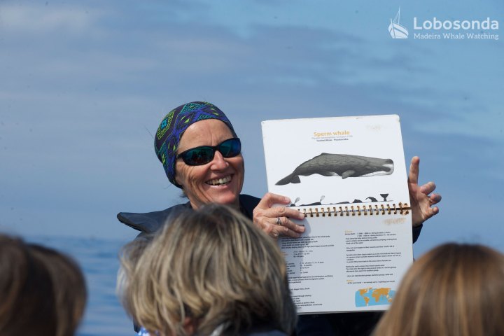 Woman showing a whale book page to people on a boat tour.